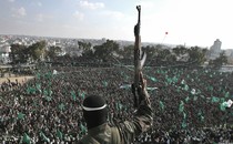 A militant, photographed from behind, holds a gun in the air as he stands before a crowd waving green flags